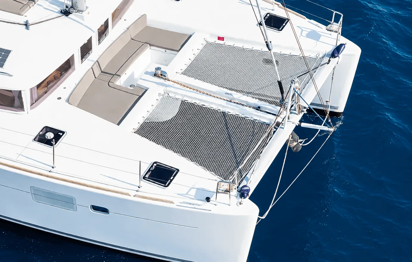 The bow of a sailing catamaran seen from above over deep blue open water, away from the coast