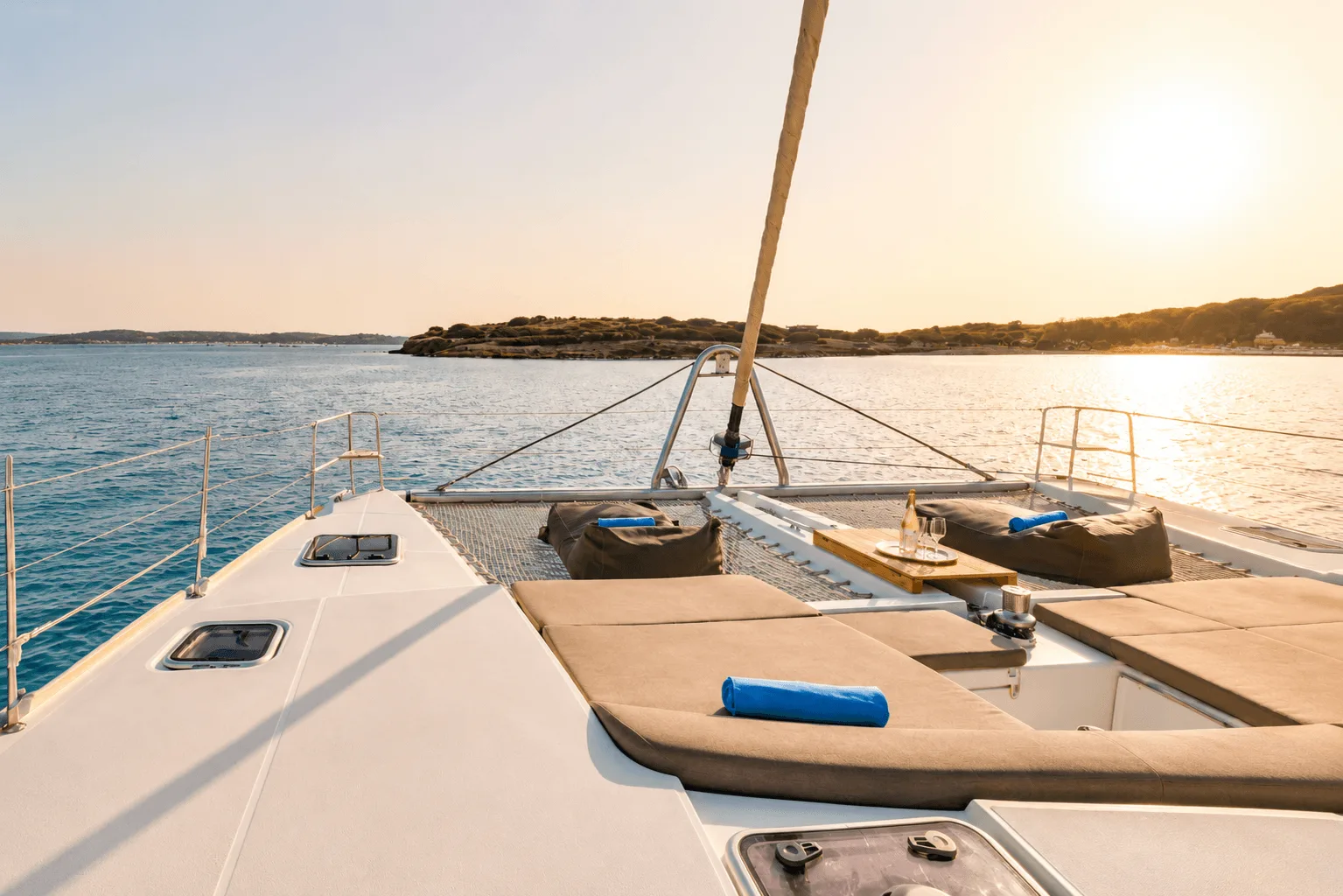 Foredeck of a sailing catamaran at sunset with a Greek island on the horizon